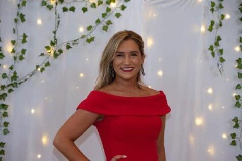 W&J junior Alyssa Pollice stands in front of while backdrop in red dress and smiles.